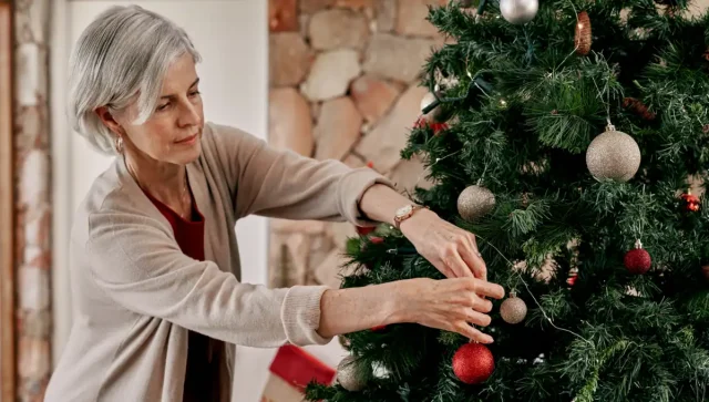 Elderly woman decorating a Christmas tree. 