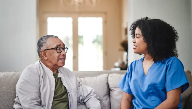 Nurse sitting on the sofa with her senior patient during home health visit.