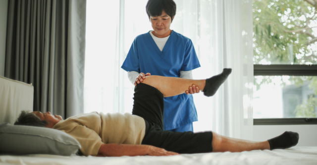 Physical therapist helping elderly woman at home with physical therapy.
